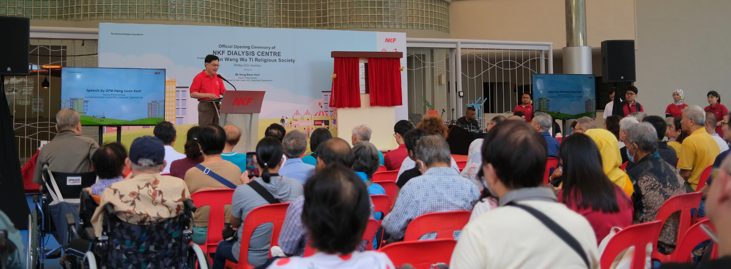 Audience at NKF event, speaker at podium, "NKF DIALYSIS CENTRE" banner.